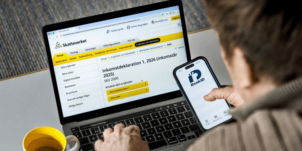 En man framför en dator med mobil i handen genomför en deklaration.