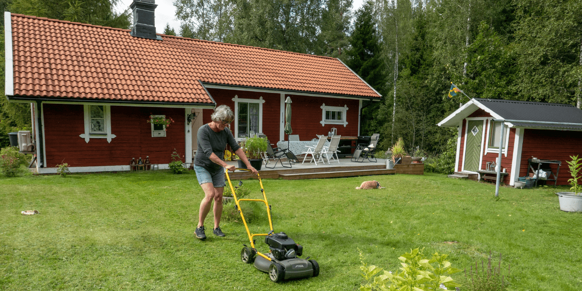 En kvinna klipper gräset framför sitt fritidshus.