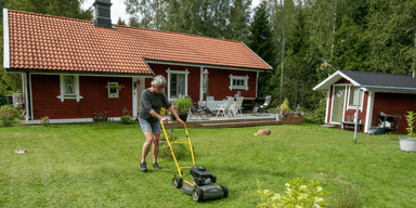 En kvinna klipper gräset framför sitt fritidshus.