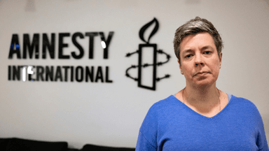 En kvinna framför en vägg det står Amnesty på.