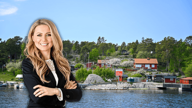 En kvinna med armarna i kors framför flera fritidshus vid vattnet.